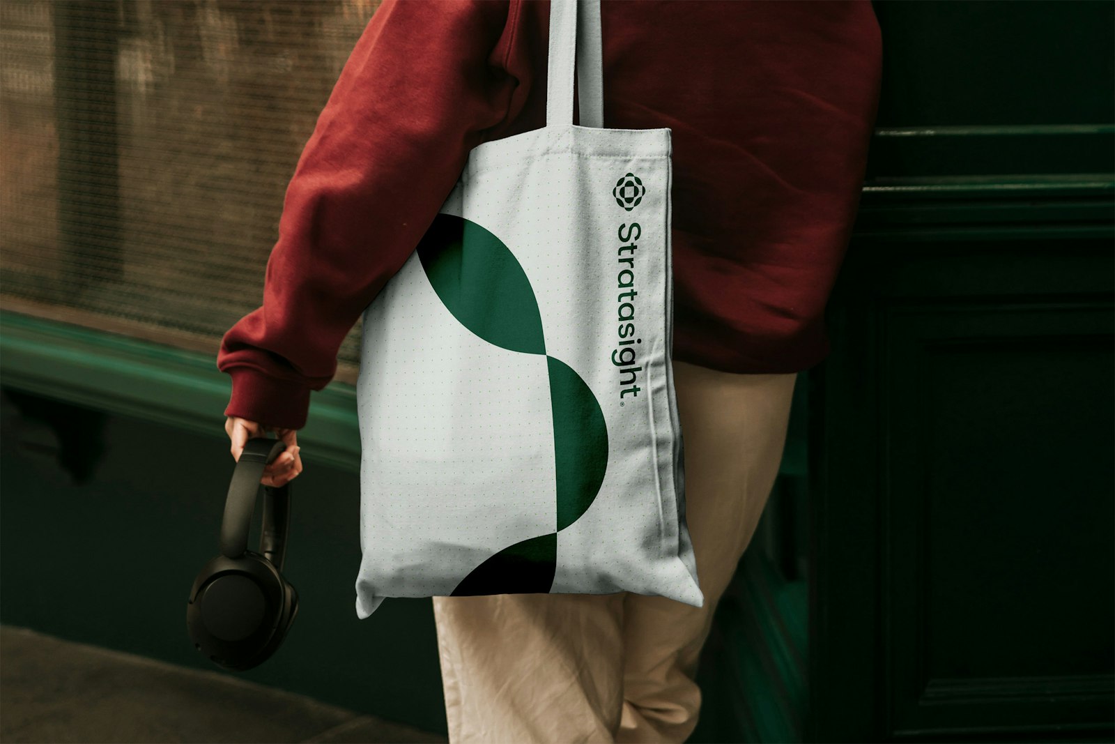 Stratasight tote bag: An example of the Stratasight logo and wordmark, developed by Capsule in Stratasight's 2026 rebrand, printed on a canvas bag slung over a person's shoulder.