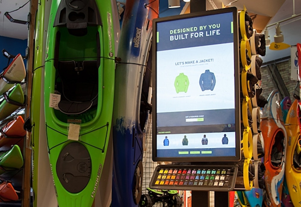 The Hexa brand recreational products kiosk with green kayak in retail display with flat screen.
